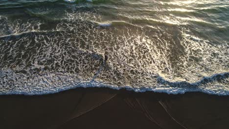 Aerial-view-top-down-of-a-man-fishing-on-a-beach-as-camera-rolls-up-to-reveal-a-beautiful-sunrise-over-a-calm-ocean