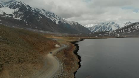 Aerial-View-Of-SUV-Driving-Going-Along-Winding-Road-Beside-Shandur-Lake-In-Pakistan