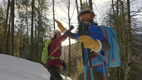 Skiing-man-and-woman-high-five-each-other-in-cold-forest