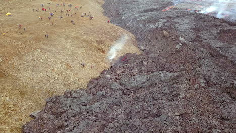 Drone-shot-of-cooling-lava-with-people-close-by-watching-the-volcano