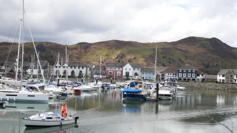 Fishing-boat-cruises-past-yachts-and-sailboats-moored-under-luxury-Conwy-mountainous-marina-waterfront-North-Wales