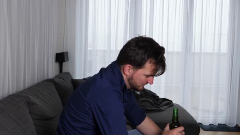 Young-alcoholic-opening-a-bottle-of-beer-and-lean-back-on-his-couch