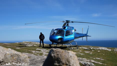 Private-tour-helicopter-on-mountain-cliff-summit-overlooking-blue-ocean-landscape-preparing-for-takeoff