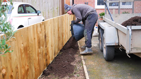 Professional-Landscape-Gardner-Applying-Topsoil,-To-Finish-Off-The-Brand-New-Fence