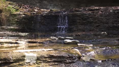 An-Sonnigen-Tagen-Fließt-Wasser-über-Eine-Kleine-Felswand-In-Den-Bach