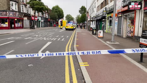 Police-officers-and-paramedics-attend-the-scene-of-a-murder-behind-crime-scene-cordon-tape-on-a-street-in-East-London