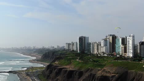 4k-daytime-aerial-video-looking-over-the-coastal-hills,-park-and-buildings-in-Lima,-in-the-touristic-area-of-Miraflores,-Peru-in-a-summer-day
