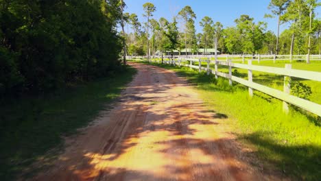 A-drone-flying-along-a-path-leading-up-to-a-beutiful-horse-ranch-with-white-picket-fences