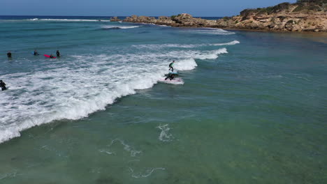 Umlaufende-Antenne-Eines-Jungen-Surfschülers,-Der-Eine-Kleine-Grüne-Uferwelle-Fängt