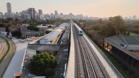 Luftaufnahme-Des-Vorbeifahrenden-Zuges-Der-Mitra-Linie-Mit-Der-Skyline-Von-Buenos-Aires-Im-Hintergrund-Bei-Sonnenuntergang
