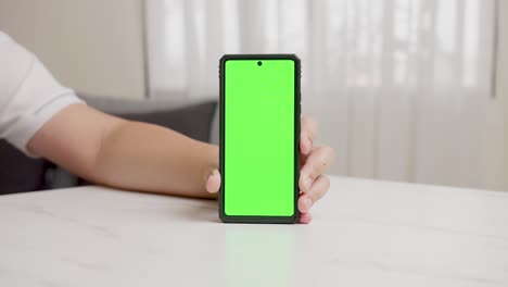 Die-Hand-Des-Mannes-Zeigt-Ein-Mobiles-Smartphone-Mit-Grünem-Bildschirm-In-Vertikaler-Position-Isoliert-Auf-Grünem-Hintergrund
