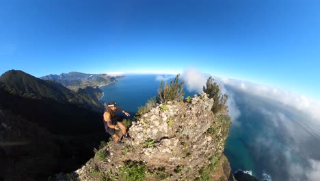 A-young-and-strong-solo-hiker-is-walking-along-the-steep-edge-of-Espigao-Amorelo-in-Madeira-with-a-360-action-camera-on-a-selfie-stick-with-an-amazing-view-of-the-landscape-and-ocean-beneath-him