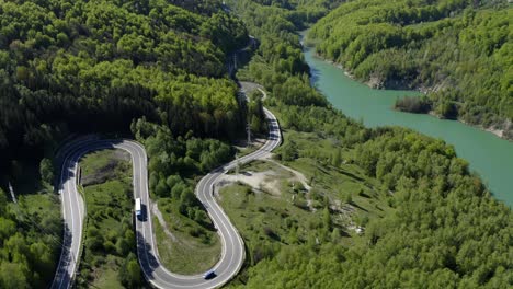 Aerial-view-of-winding-mountain-road-through-the-forest-on-lakeshore
