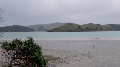 Watching-the-ocean,-mudflats-and-tidal-coastal-scene-on-a-moody,-grey,-overcast-and-blustery-day-in-the-small-town-of-Raglan,-Waikato,-New-Zealand