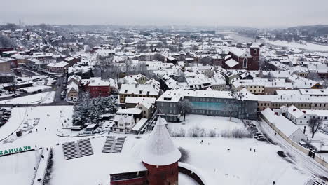 Kaunas-city-skyline-and-medieval-castle-during-winter-season-and-snowstorm,-aerial-view