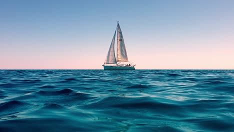 Zoom-in-and-low-angle-sea-level-view-of-small-yacht-boat-sailing-in-calm-open-sea-at-sunset