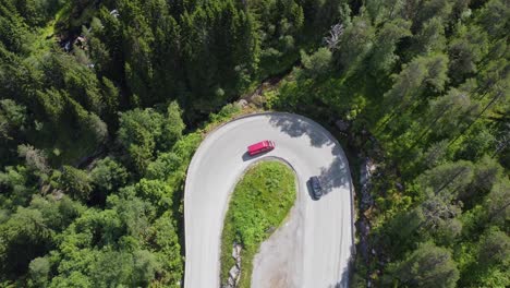 Winding-roads-at-E39-Førde-Norway---Ascending-top-down-aerial-of-180-degree-curve-with-traffic-climbing-up-mountain-inside-evergreen-forest