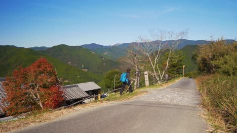 Static,-female-walks-path-through-village-in-lush-mountain-landscape-,-Japan