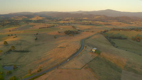 Two-cars-traveling-along-vast-country-side-highway-during-majestic-autumn-evening-dusk-light-in-Yarra-Valley,-Victoria,-Australia