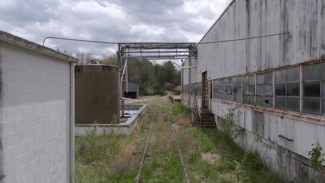 Drone-Footage-Pushing-Forwards-Over-Some-Overgrown-Train-tracks-in-an-Abandoned-Factory