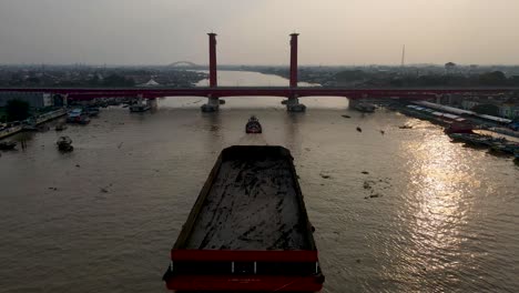 Massive-industrial-barge-sailing-under-Ampera-bridge,-aerial-drone-view