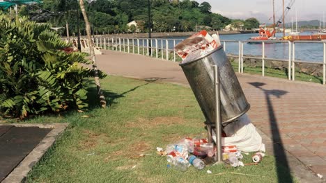 An-overflowing-public-trash-bin-along-a-coastal-promenade,-plastic-bottles,-bags-and-non-biodegradable-waste-have-a-devastating-environmental-impact,-Causeway-of-Amador,-Panama-City