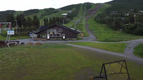 Fuera-De-Temporada-En-Ski-geilo-Noruega---Antena-En-Movimiento-Hacia-Adelante-Cerca-Del-Suelo-Con-Pistas-De-Esquí-Verdes-En-El-Fondo