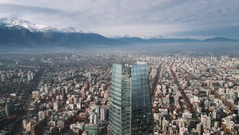 Close-up-aerial-view-of-an-orbit-with-buildings-in-Santiago,-Chile-and-the-snow-capped-Andes-Mountains-in-winter