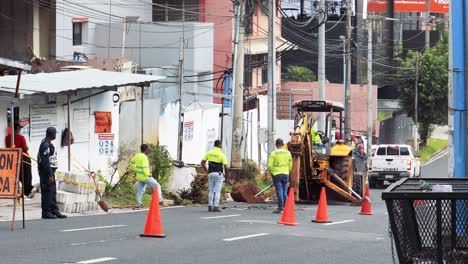 Men-watch-a-hydraulic-breaker-bulldozer-break-asphalt,-Panama-City,-Panama,-wide,-Road-digging-to-repair-or-replace-water-pipes