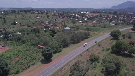 Aerial-tracks-transit-bus-on-highway-entering-town-in-Malawi,-Africa