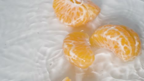Nahaufnahme-Geschälte-Mandarine-Fällt-Ins-Wasser-Und-Zerfällt-In-Scheiben,-Weißer-Hintergrund