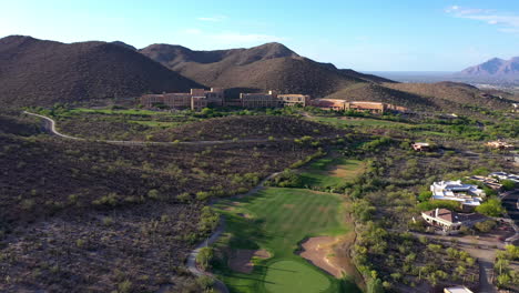 Aerial-forward-over-golf-course-towards-JW-Marriott-Starr-Pass-resort-and-mountains-in-background,-Arizona