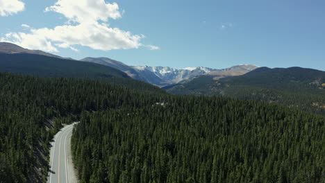 Aerial-view-moving-from-forest-highway-to-alpine-lake-to-mountain-range,-4K