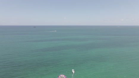 Aerial-flight-over-colorful-parasail-and-boat-in-shallow-green-water