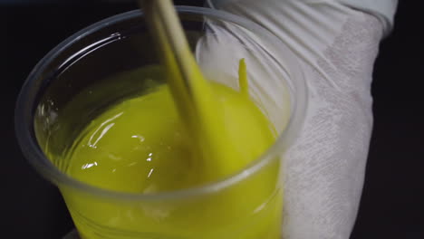 Close-up,-hands-with-white-gloves-mixing-thick-viscous-yellow-liquid-with-sticks