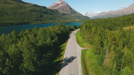 Car-Driving-Across-Country-Road-In-Coniferous-Forest-With-Hills-And-Alps-Background-Near-Tromso,-Northern-Norway