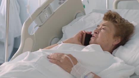 Elderly-Female-Patient-Lying-On-The-Hospital-Bed-And-Talking-On-Her-Cellphone