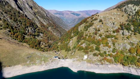 Lac-d'Oô-dam-wall-and-keeper's-cabins-in-the-French-Pyrenees-in-the-daytime,-Aerial-high-approach-shot