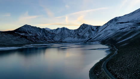 Reflejo-Del-Lago,-Carretera-Costera-Y-Majestuosa-Cordillera-Nevada,-Vista-Aérea-De-Drones