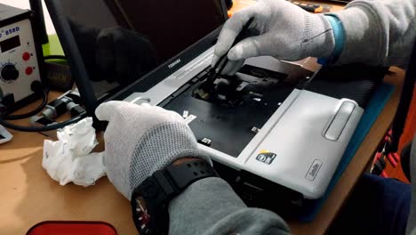 Gloved-Male-Hands-Of-Engineer-Repairing-Laptop-On-Wooden-Desk