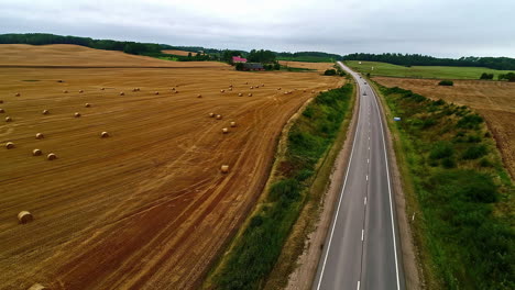 Vehicles-Driving-On-Long-Asphalt-Highway-Through-Farmland-With-Rolls-Of-Hay-Bales