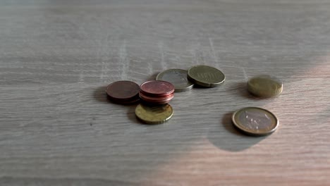 Multiple-Euro-and-Cent-coins-being-put-on-a-wooden-interior-table