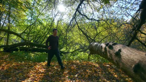 A-Young-Active-Man-Jumping-Over-The-Big-Tree-Trunk-During-Fall-Season-In-Lithuania,-Europe--Tracking-Shot