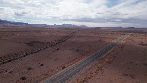 Drone-shot-of-a-railroad-and-highway-in-the-desert-with-one-car-on-the-road
