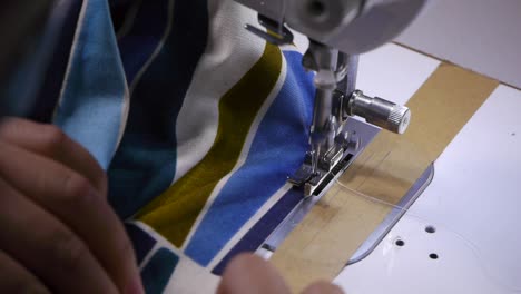 Close-up-of-on-hands-pushing-cloth-with-patterns-through-sewing-machine-to-add-stitches-on-edge-of-fabric