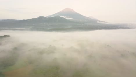 Cinematic-drone-panoramic-of-beautiful-indonesian-scenery-with-hovering-clouds-and-mist-during-sunny-day---Silhouette-of-Mount-Sumbing-in-background---Sun-flares-lighting-during-daytime