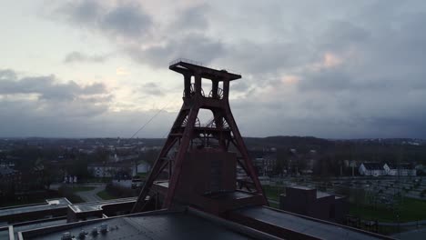 Shaft-XII-winding-tower-mining-headframe-at-Zeche-Zollverein,-wheels-turning,-drone-aerial