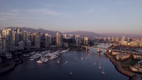 Aerial-forward-over-False-Creek-with-mountain-range-in-background-at-sunset,-Vancouver-in-Canada