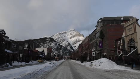 Conduciendo-A-Lo-Largo-De-La-Avenida-Banff-Con-La-Montaña-Cascada-En-La-Distancia,-Paisaje-Invernal,-Punto-De-Vista-De-Cámara-Lenta