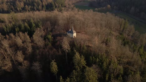 Aerial-footage-of-a-small-chapel-on-top-of-a-hill-that-is-covered-with-dry,-brown-trees